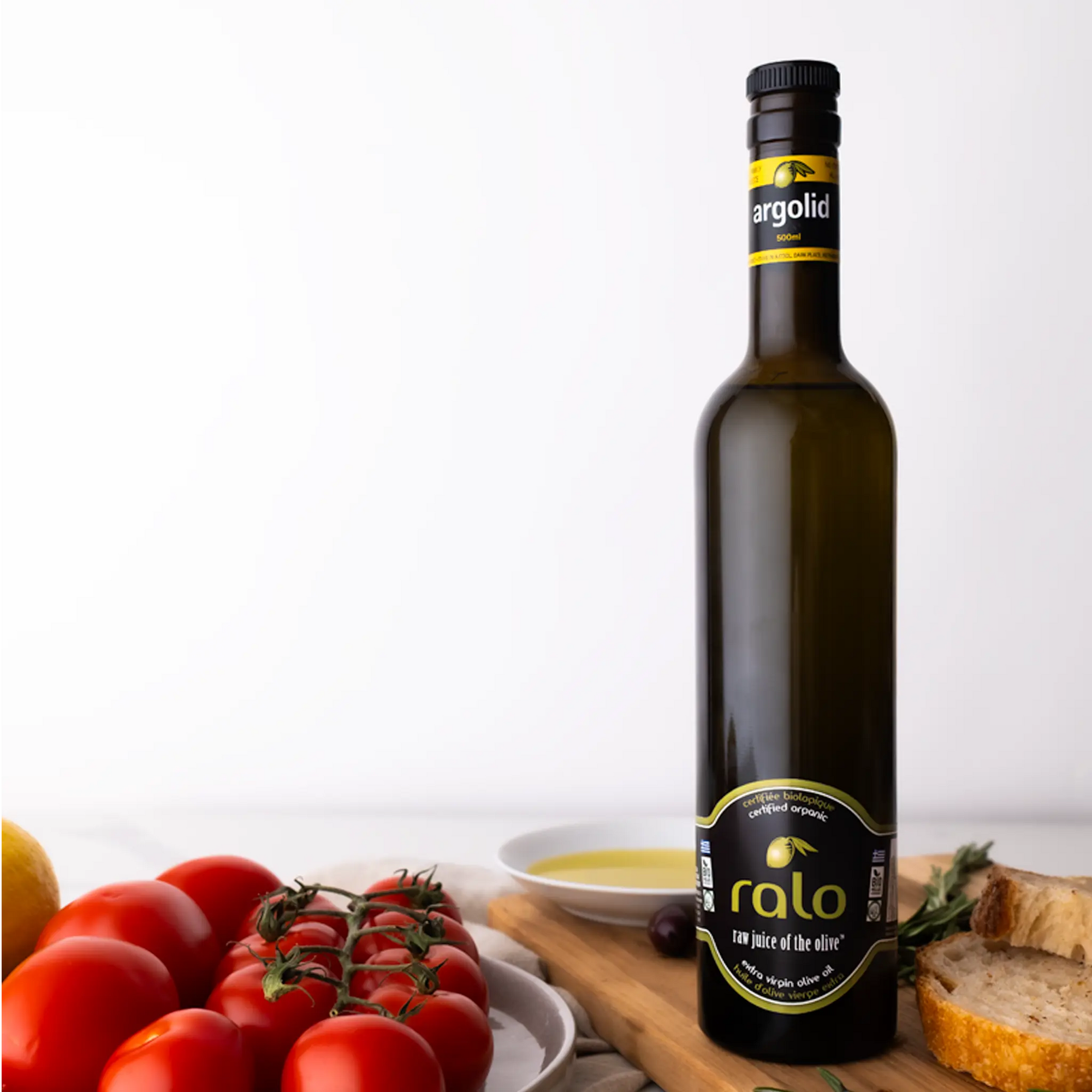 Bottle of Argolid olive oil with tomatoes and bread on a wooden board