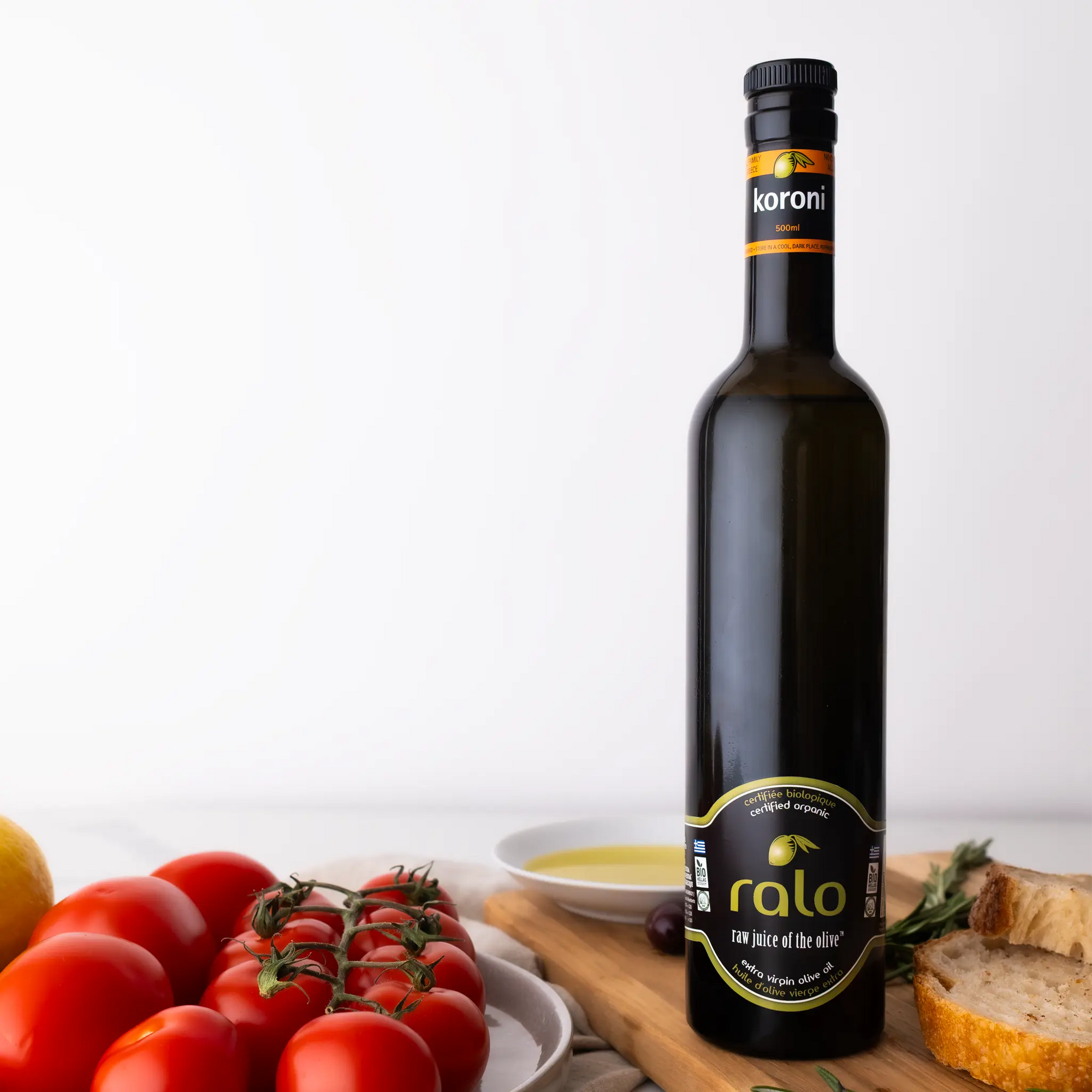 Bottle of Koroni olive oil on a wooden cutting board with tomatoes and bread.