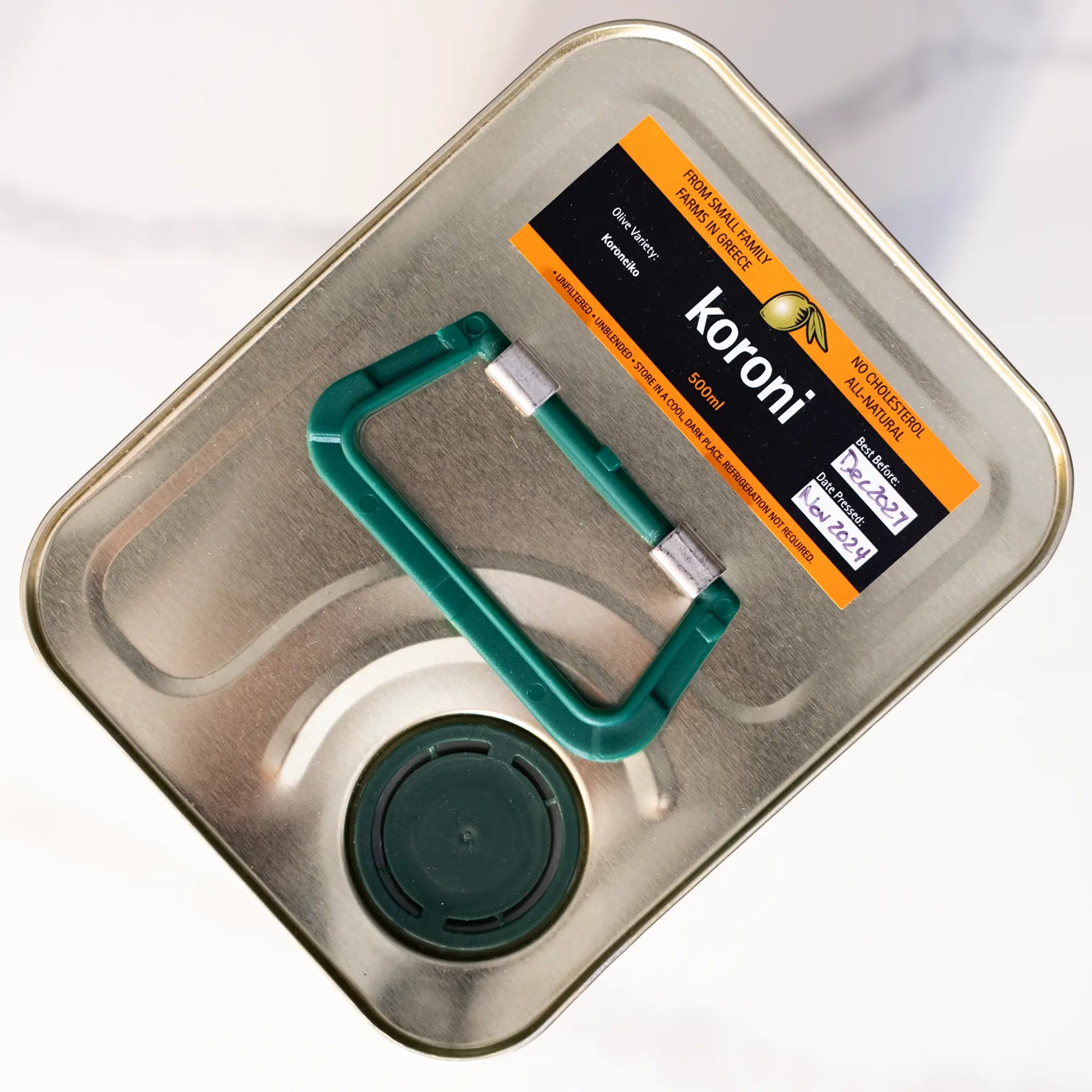 Top of metal tin with green handle, pouring spout, and 'koroni' olive oil sticker.